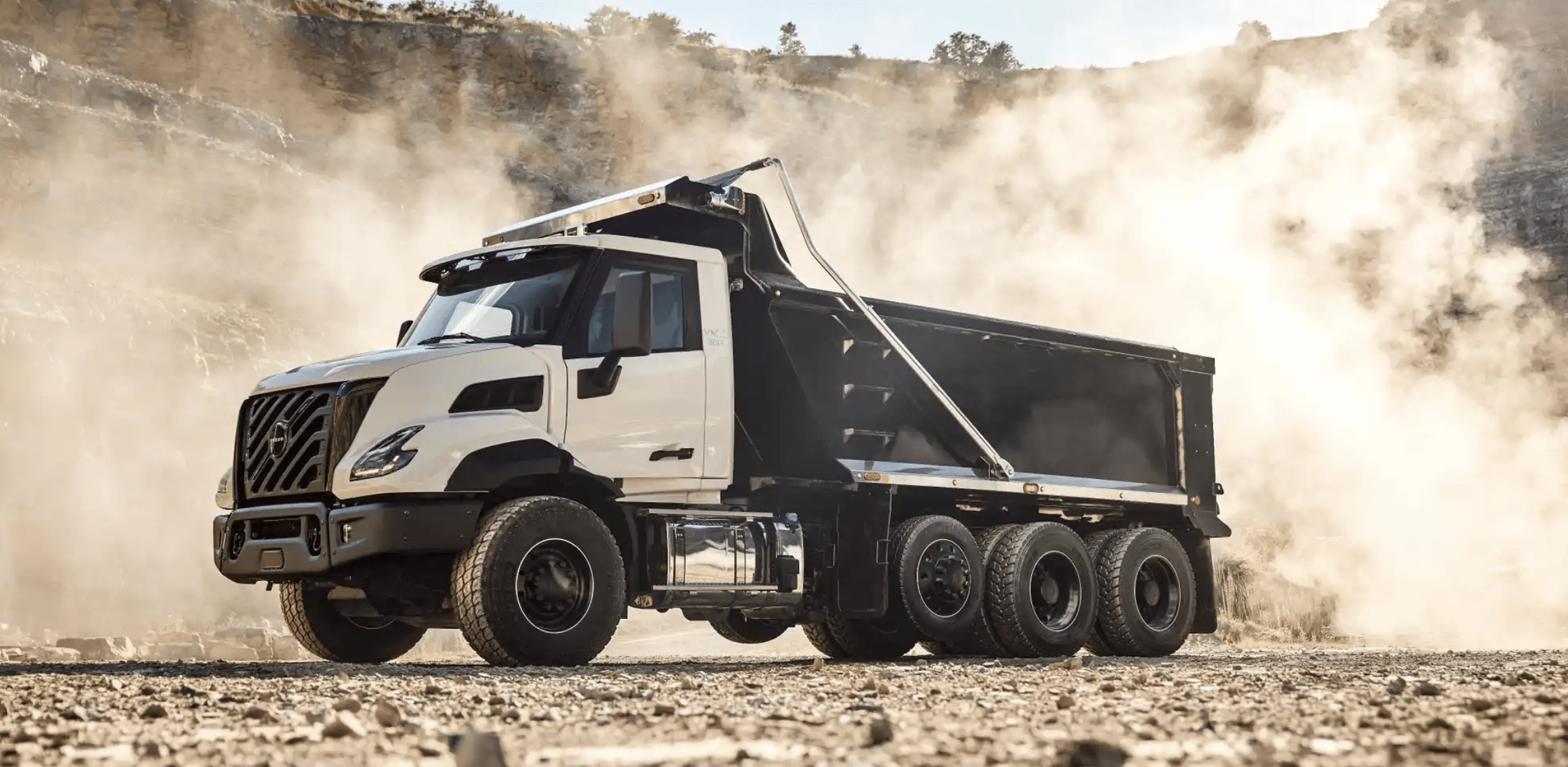 White Volvo VNX dump truck with a black dump body kicking up dust in a quarry