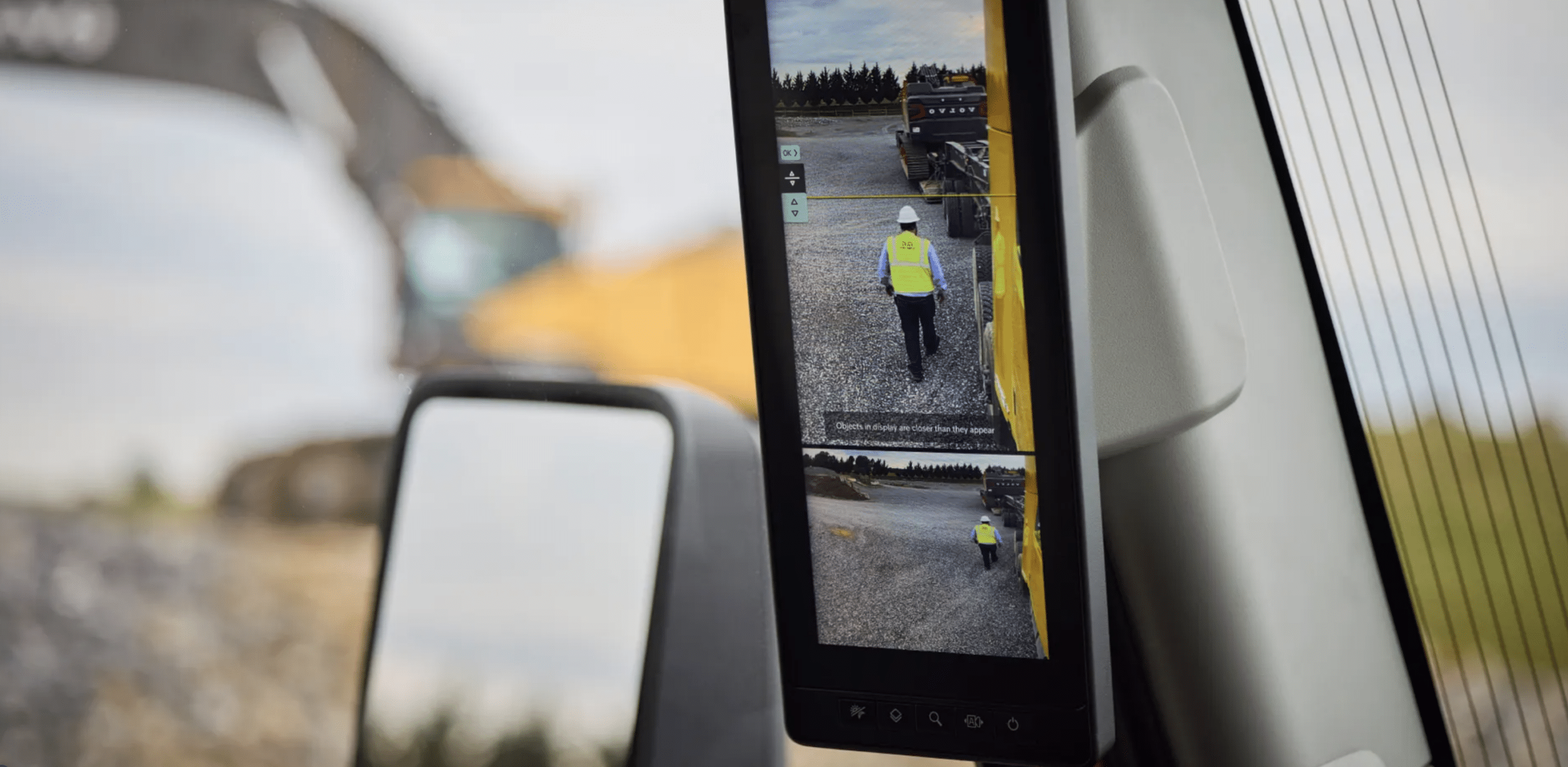 Camera Monitor System display mounted on the A-pillar showing a worker walking beside the truck