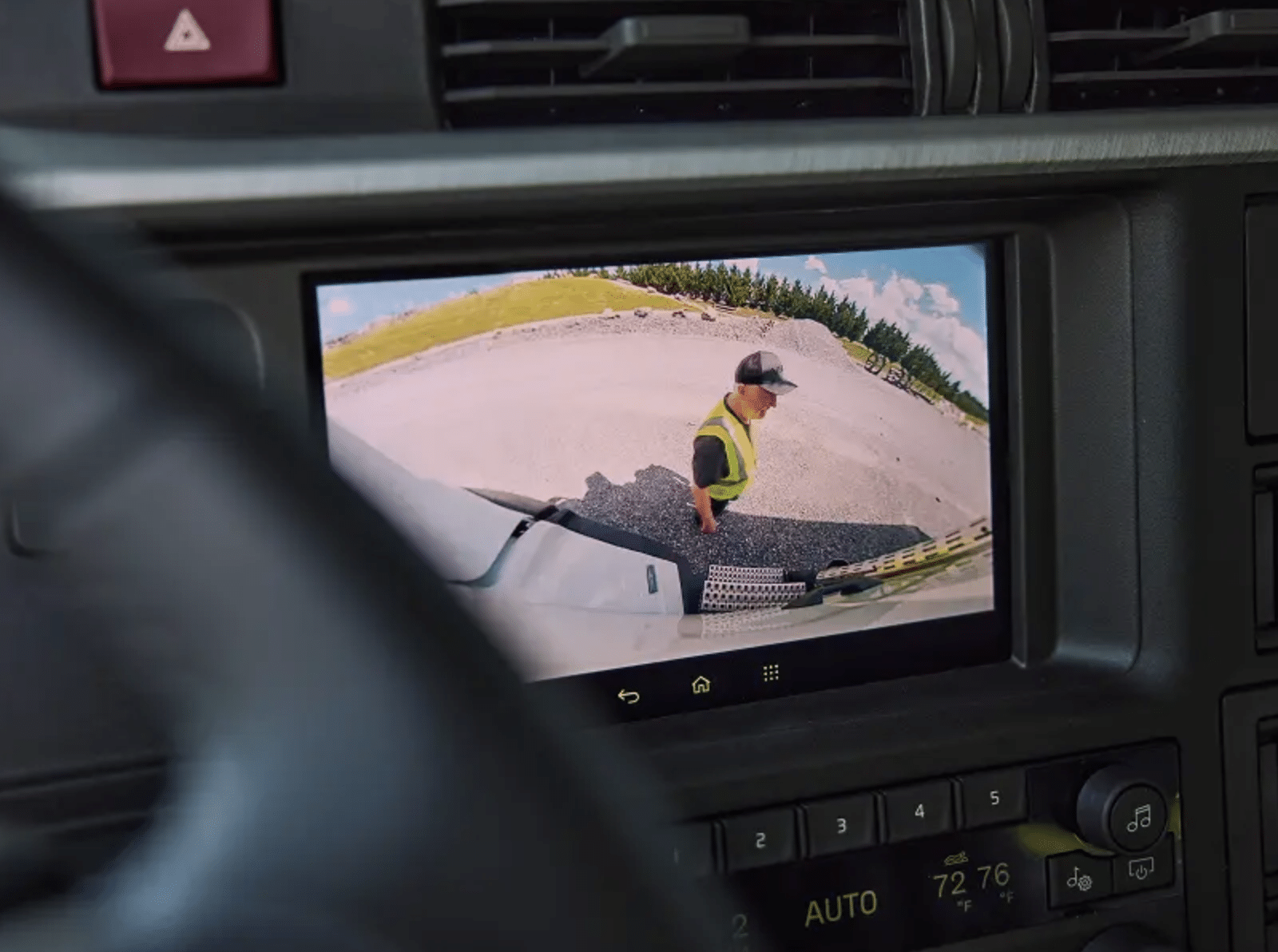 Infotainment screen showing a camera view of a worker near the front of the truck