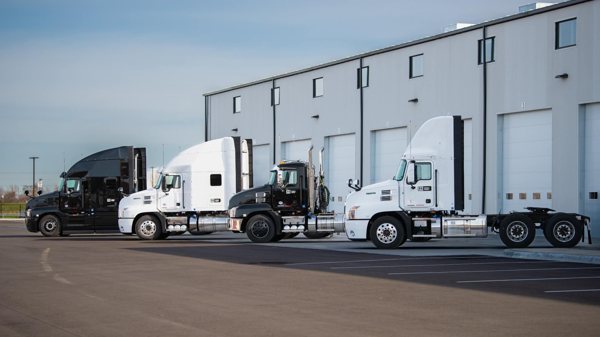 Row of Nuss Lease & Rental Mack tractors parked beside a Nuss service building