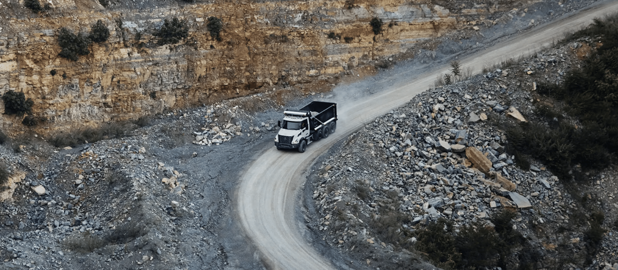 Aerial view of a white VNX dump truck climbing a winding quarry haul road